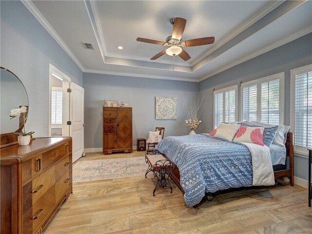 bedroom featuring multiple windows, a tray ceiling, light hardwood / wood-style floors, and crown molding