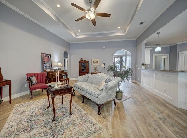 living room with ornamental molding, a raised ceiling, ceiling fan, and light wood-type flooring