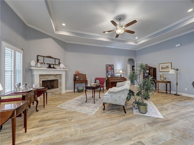 sitting room featuring a stone fireplace, ornamental molding, ceiling fan, a tray ceiling, and light hardwood / wood-style flooring