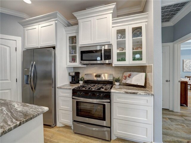 kitchen with light stone counters, ornamental molding, appliances with stainless steel finishes, decorative backsplash, and white cabinets