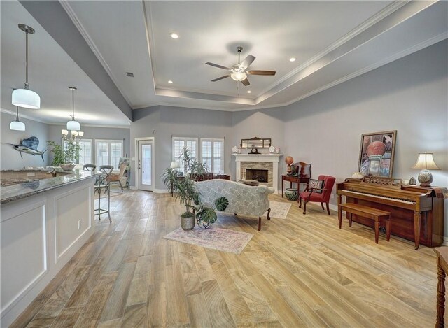 living room featuring ornamental molding, a premium fireplace, a raised ceiling, and light hardwood / wood-style flooring