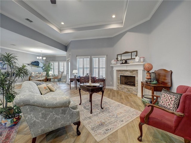 living room featuring crown molding, a stone fireplace, hardwood / wood-style floors, and a tray ceiling