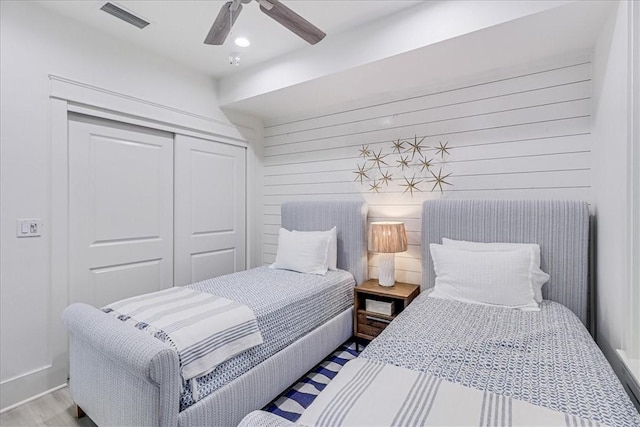 bedroom featuring a closet, visible vents, ceiling fan, wood walls, and wood finished floors