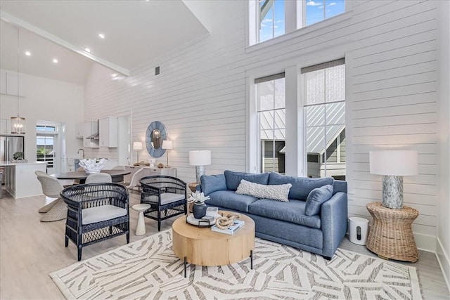 living room featuring a towering ceiling, light wood-style flooring, and a notable chandelier