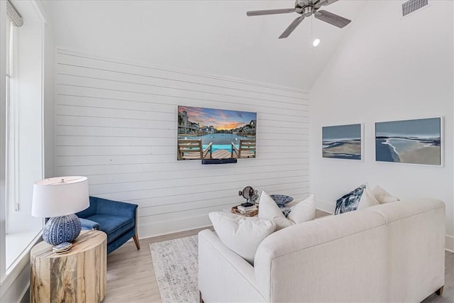 living room with visible vents, a ceiling fan, lofted ceiling, wood finished floors, and wood walls