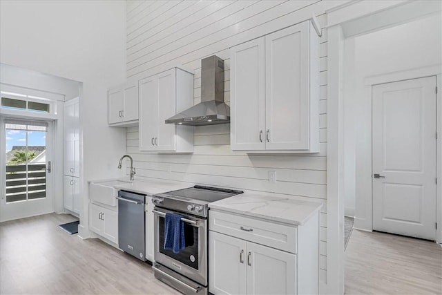 kitchen featuring light wood-style floors, light stone counters, stainless steel appliances, wall chimney range hood, and a sink