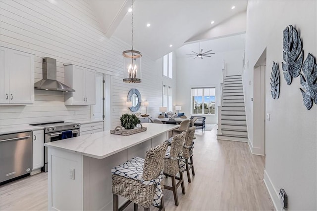 kitchen featuring a breakfast bar area, light wood-style floors, open floor plan, wall chimney range hood, and appliances with stainless steel finishes