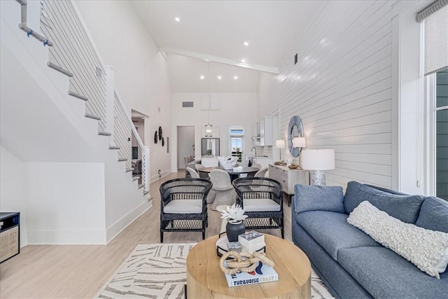 living area featuring baseboards, visible vents, stairway, a high ceiling, and light wood-type flooring