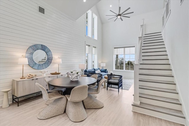 dining area featuring a towering ceiling, a ceiling fan, stairway, and wood finished floors