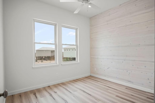 spare room with wooden walls, plenty of natural light, ceiling fan, and light hardwood / wood-style floors