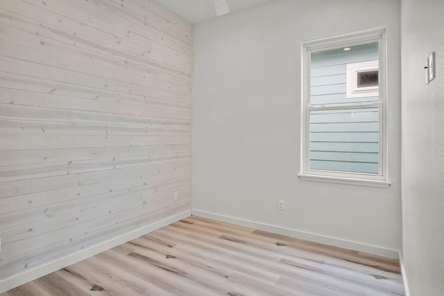 empty room with a healthy amount of sunlight, light wood-type flooring, and wooden walls