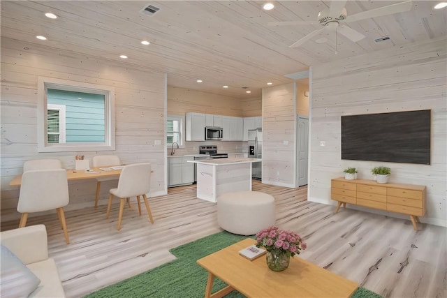 living room with ceiling fan, light hardwood / wood-style flooring, wood ceiling, and wood walls