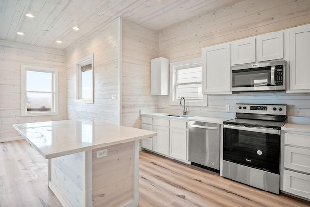 kitchen with white cabinets, sink, wooden walls, light wood-type flooring, and appliances with stainless steel finishes