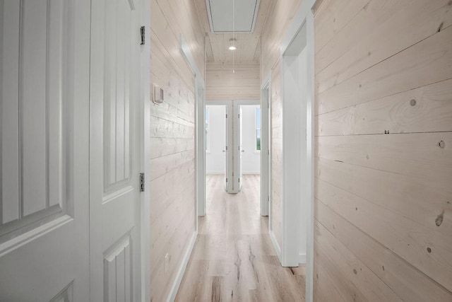 corridor with light wood-type flooring and wooden walls