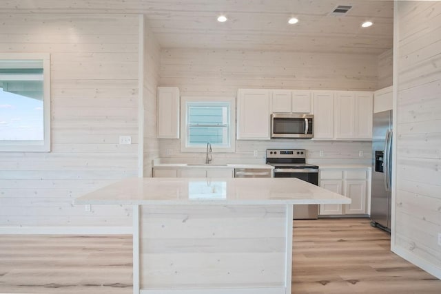 kitchen featuring wooden walls, a center island, white cabinets, and stainless steel appliances