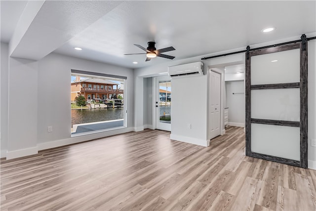 unfurnished living room with an AC wall unit, a textured ceiling, a barn door, ceiling fan, and light hardwood / wood-style flooring