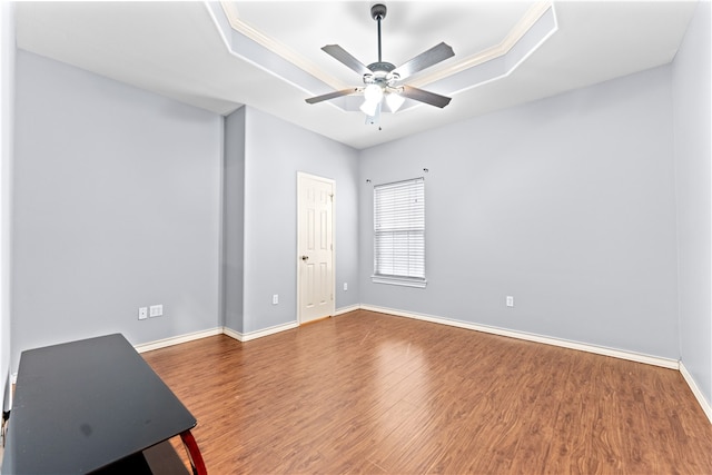 empty room with hardwood / wood-style floors, ceiling fan, and a raised ceiling