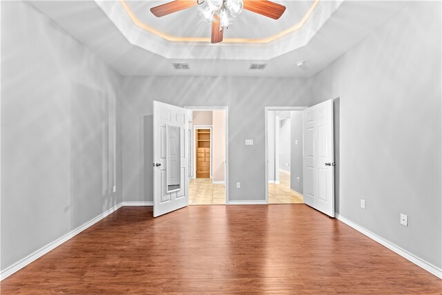 unfurnished bedroom with ornamental molding, light hardwood / wood-style flooring, ceiling fan, and a tray ceiling