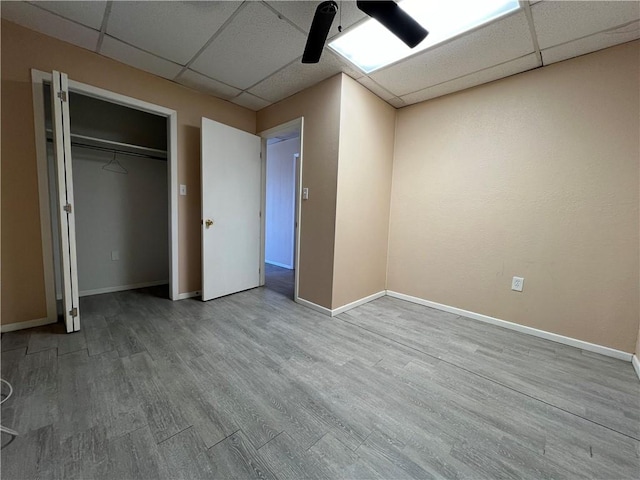 unfurnished bedroom with light hardwood / wood-style flooring, ceiling fan, a drop ceiling, and a closet