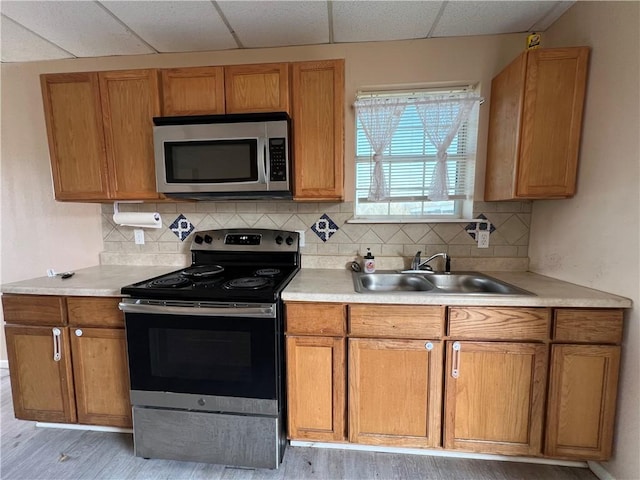 kitchen featuring stainless steel appliances, light hardwood / wood-style floors, sink, backsplash, and a drop ceiling