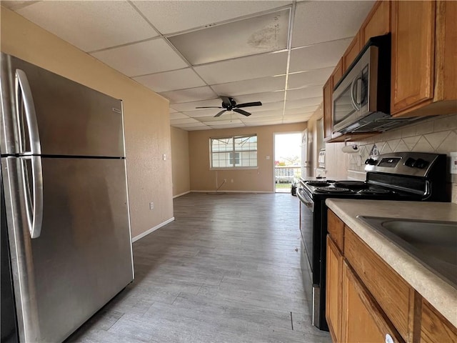 kitchen with stainless steel appliances, light hardwood / wood-style floors, ceiling fan, decorative backsplash, and a drop ceiling