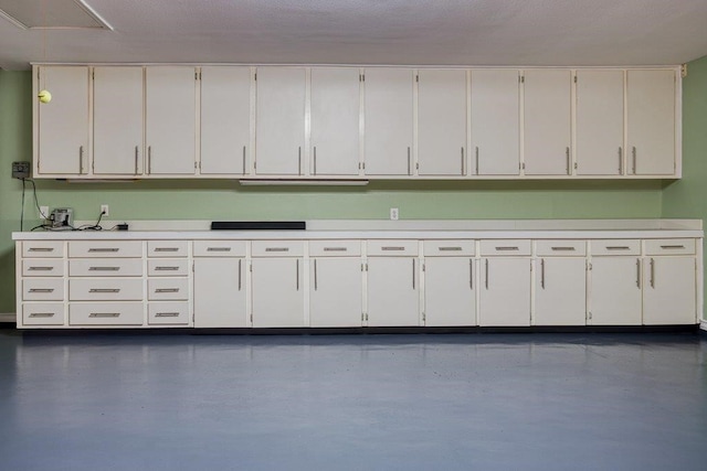 interior space featuring finished concrete flooring, white cabinets, and light countertops