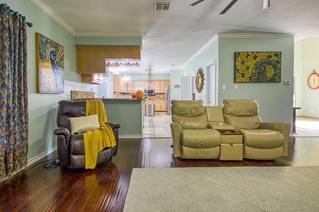 living area with baseboards, crown molding, visible vents, and hardwood / wood-style floors