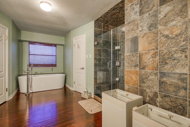 full bath with baseboards, wood finished floors, a tile shower, a textured ceiling, and a freestanding tub