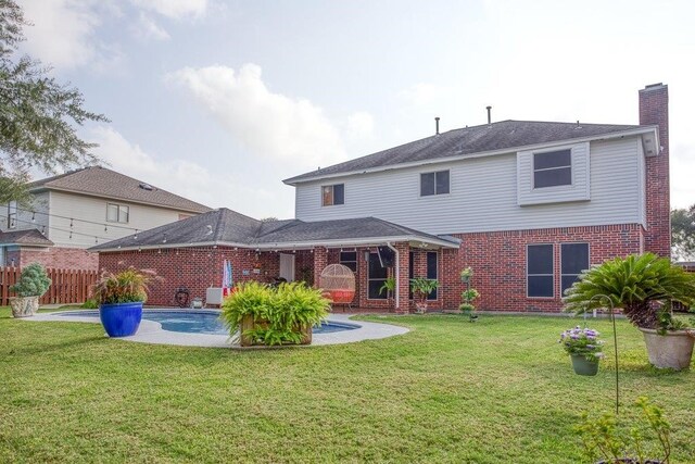 rear view of house featuring brick siding, a lawn, fence, and a fenced in pool