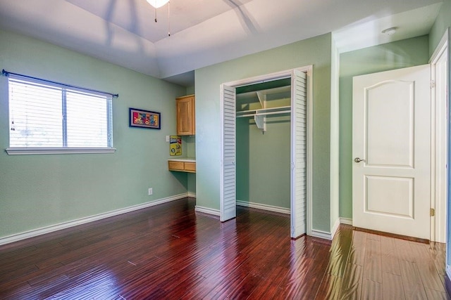 unfurnished bedroom featuring a closet, baseboards, wood finished floors, and built in study area