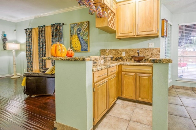 kitchen featuring ornamental molding, baseboards, a peninsula, and light stone counters