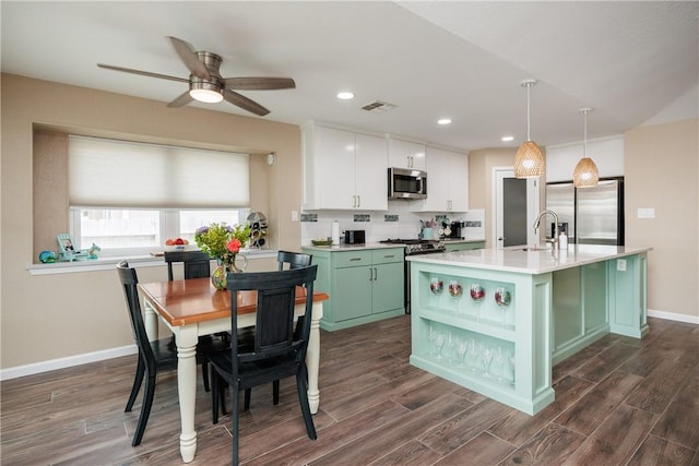 kitchen with appliances with stainless steel finishes, a kitchen island with sink, white cabinetry, hanging light fixtures, and green cabinets