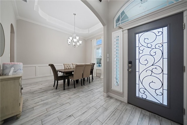 foyer with arched walkways, a raised ceiling, a decorative wall, light wood-style floors, and ornamental molding