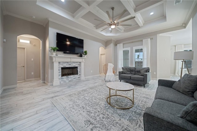 living area with arched walkways, ceiling fan, coffered ceiling, light wood-style floors, and a tiled fireplace