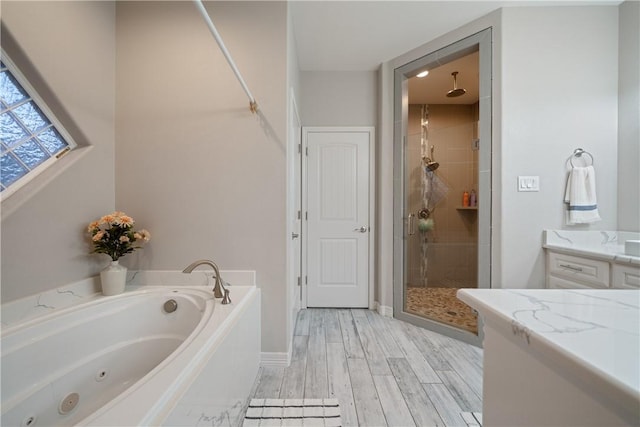 bathroom with a stall shower, baseboards, vanity, a jetted tub, and wood finish floors