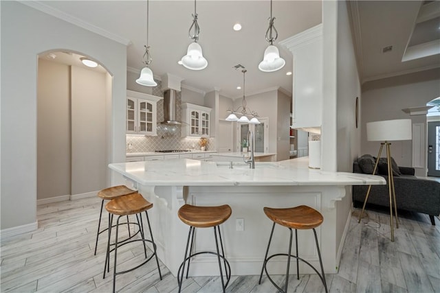 kitchen featuring decorative backsplash, white cabinetry, wall chimney range hood, and a kitchen breakfast bar