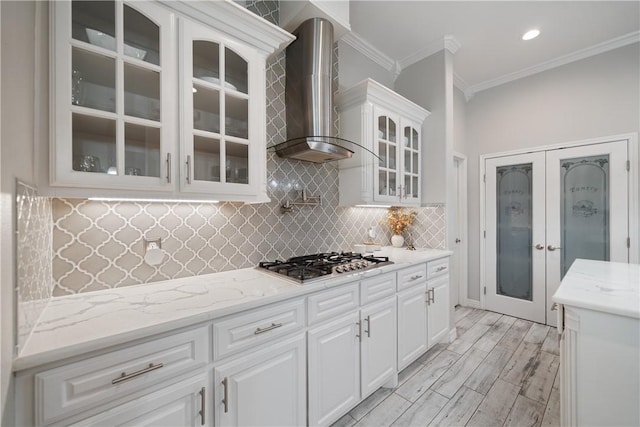 kitchen with white cabinets, glass insert cabinets, crown molding, wall chimney range hood, and stainless steel gas stovetop