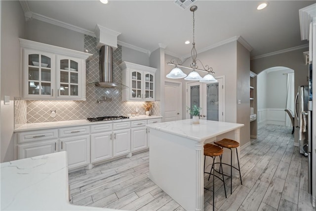 kitchen with arched walkways, gas cooktop, white cabinets, light wood-style floors, and wall chimney range hood