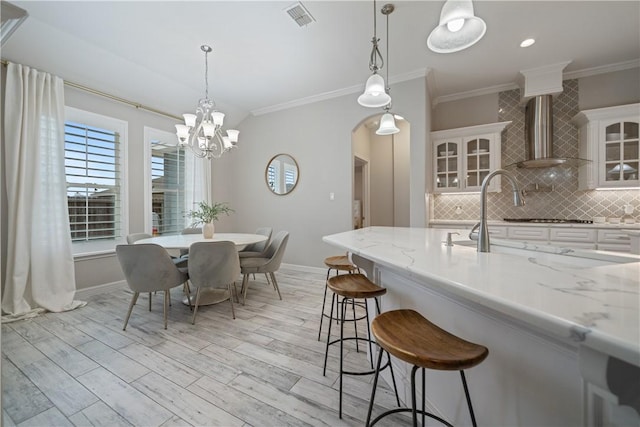 kitchen featuring a breakfast bar, arched walkways, visible vents, backsplash, and wall chimney range hood