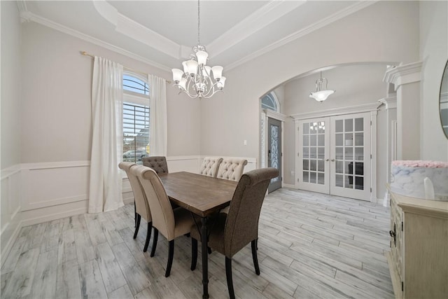 dining area featuring a chandelier, arched walkways, light wood-type flooring, wainscoting, and a raised ceiling