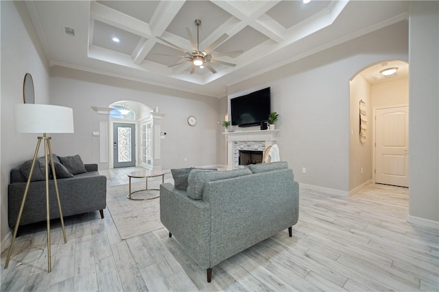 living room with arched walkways, coffered ceiling, a tile fireplace, and light wood-style flooring