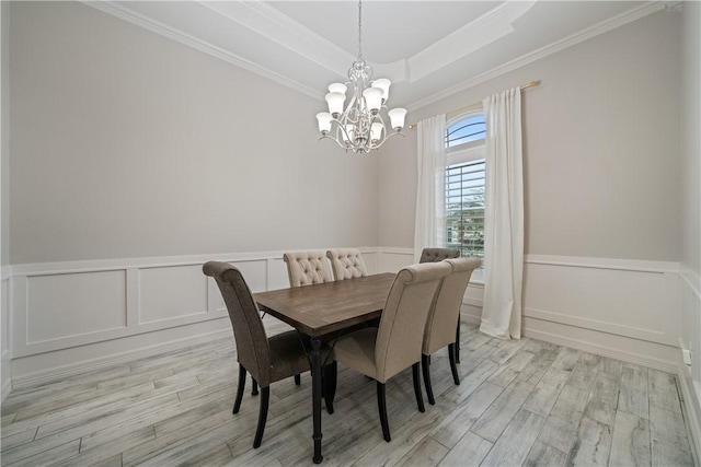 dining space featuring a notable chandelier, a wainscoted wall, a tray ceiling, light wood finished floors, and crown molding