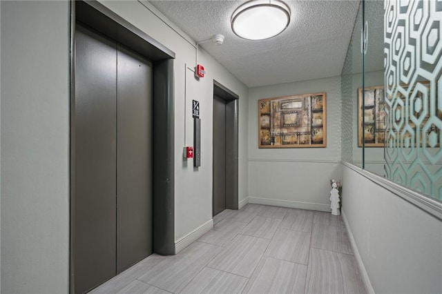 hallway featuring elevator, baseboards, and a textured ceiling