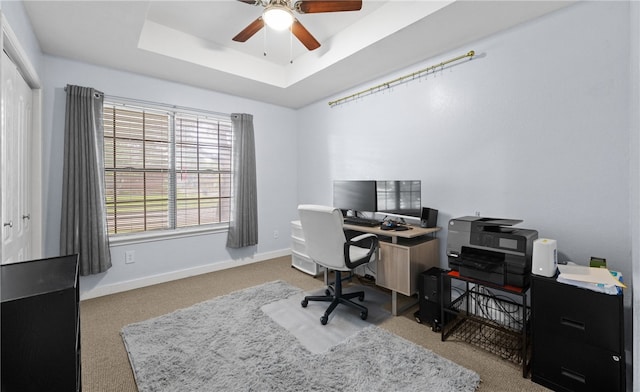 carpeted office space with ceiling fan and a raised ceiling