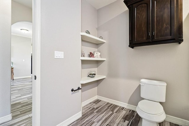 bathroom featuring baseboards, wood finished floors, and toilet