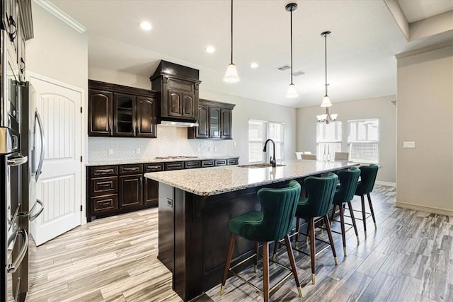 kitchen featuring a sink, stainless steel gas cooktop, an island with sink, decorative backsplash, and a kitchen bar