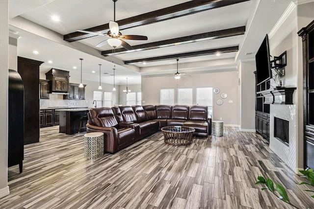 living area featuring a ceiling fan, a fireplace, light wood-type flooring, beam ceiling, and baseboards