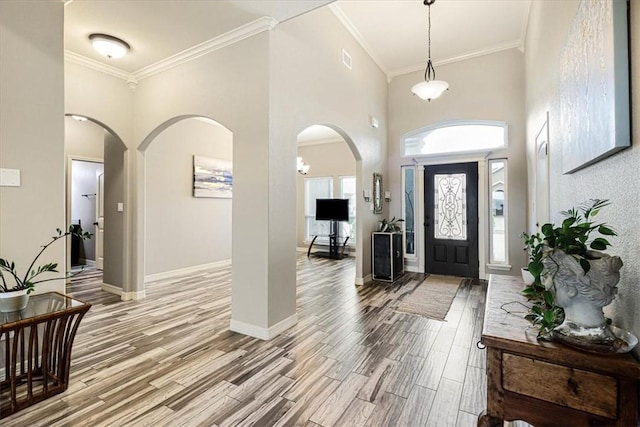 entryway featuring crown molding, baseboards, a high ceiling, light wood-type flooring, and arched walkways