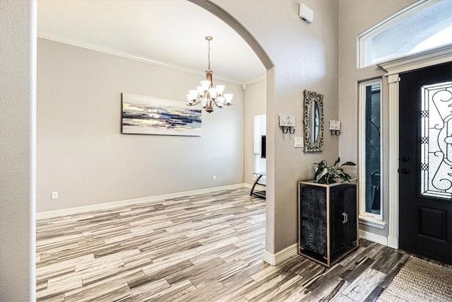 foyer entrance featuring an inviting chandelier, crown molding, wood finished floors, baseboards, and arched walkways