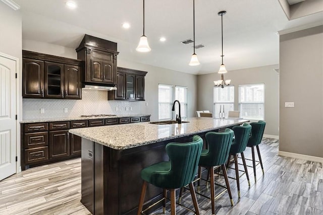 kitchen featuring a kitchen breakfast bar, a kitchen island with sink, backsplash, stainless steel gas cooktop, and a sink
